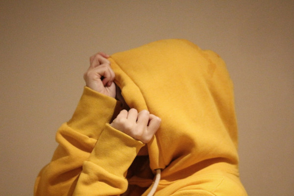 Person versteckt schamvoll ihr Gesicht in der Kapuze eines gelben Hoodies